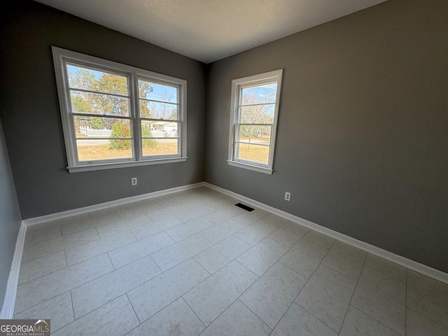 empty room with a textured ceiling, visible vents, and baseboards