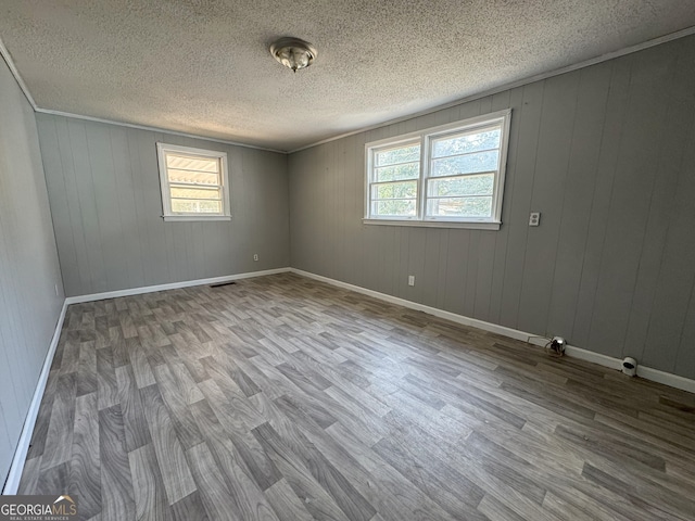 unfurnished room with baseboards, visible vents, wood finished floors, crown molding, and a textured ceiling