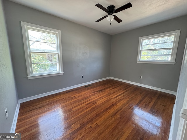 unfurnished room with dark wood-type flooring, visible vents, and baseboards