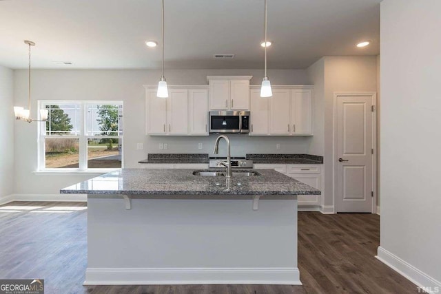 kitchen with a sink, white cabinetry, dark stone counters, stainless steel microwave, and a center island with sink