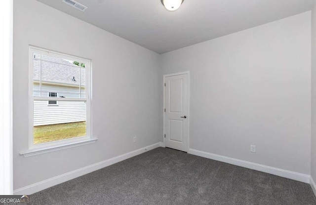 spare room with plenty of natural light, visible vents, dark colored carpet, and baseboards