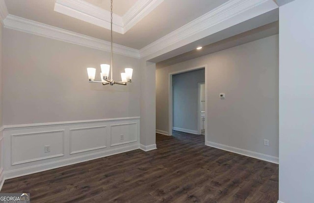 unfurnished dining area with a decorative wall, a wainscoted wall, crown molding, dark wood-style flooring, and an inviting chandelier