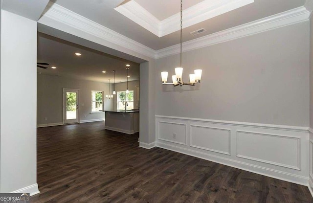 interior space with crown molding, a raised ceiling, dark wood-type flooring, wainscoting, and a chandelier