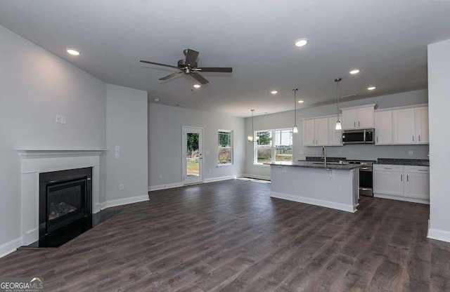 kitchen with white cabinetry, open floor plan, hanging light fixtures, appliances with stainless steel finishes, and a center island with sink