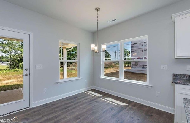 unfurnished dining area with dark wood-style floors, baseboards, visible vents, and a notable chandelier