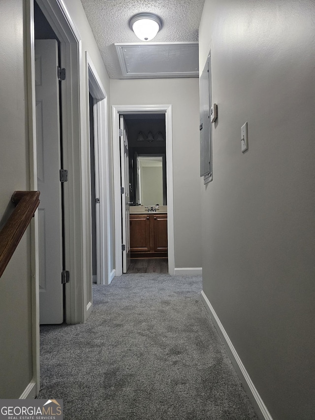 hall featuring a sink, baseboards, dark colored carpet, and a textured ceiling