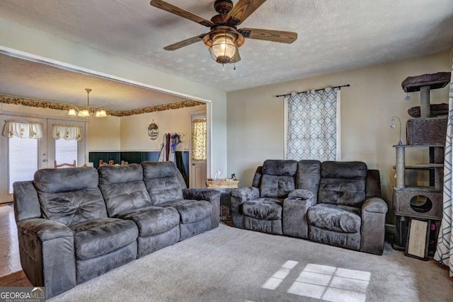 carpeted living area featuring a textured ceiling and ceiling fan with notable chandelier