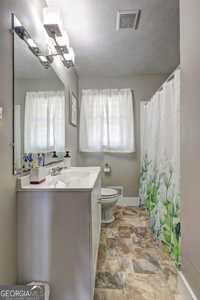 full bathroom featuring toilet, a textured ceiling, vanity, and visible vents