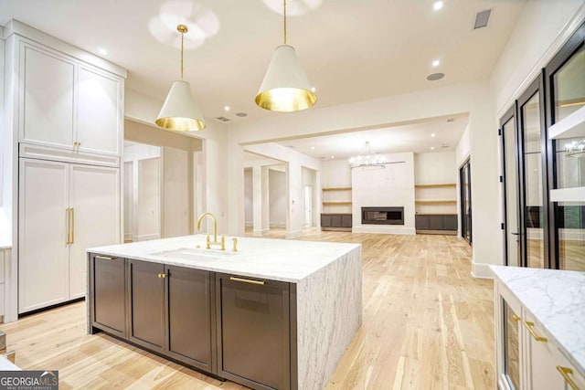 kitchen with hanging light fixtures, light stone countertops, paneled refrigerator, and a sink