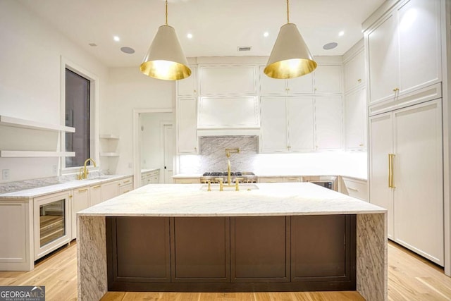 kitchen featuring wine cooler, pendant lighting, a center island with sink, white cabinets, and light wood-type flooring