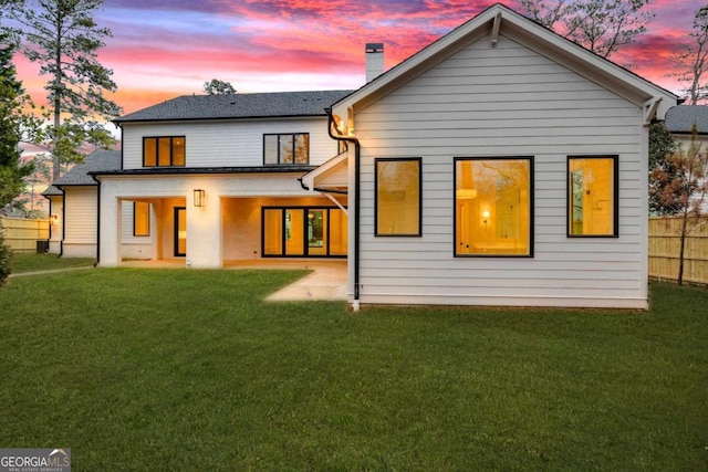 back of house at dusk with a chimney, a yard, a patio, and fence