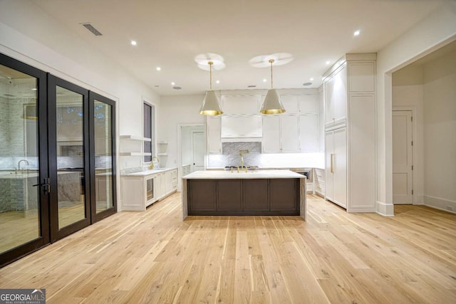 kitchen with visible vents, white cabinets, decorative light fixtures, a kitchen island with sink, and light countertops