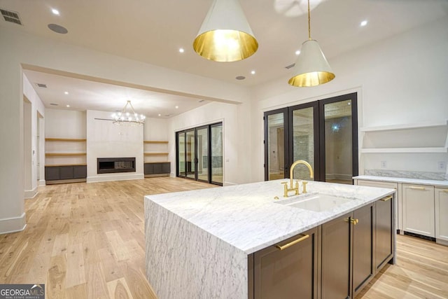 kitchen with visible vents, an island with sink, light stone counters, white cabinetry, and a sink