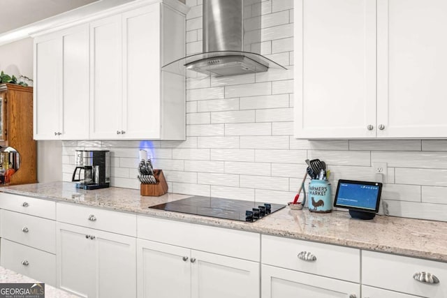 kitchen with tasteful backsplash, white cabinets, wall chimney exhaust hood, light stone countertops, and black electric stovetop