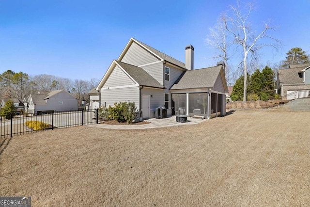 rear view of house featuring a yard, a patio, a chimney, a sunroom, and a fenced backyard