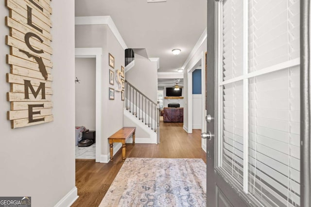 foyer with stairs, a fireplace, ornamental molding, and wood finished floors