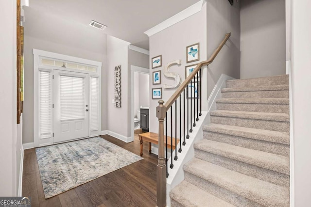 foyer entrance featuring visible vents, dark wood-type flooring, ornamental molding, baseboards, and stairs