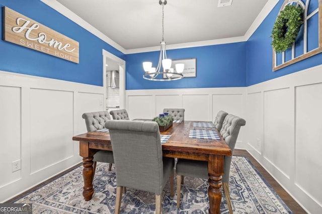 dining space featuring visible vents, wainscoting, dark wood-style flooring, a decorative wall, and a notable chandelier