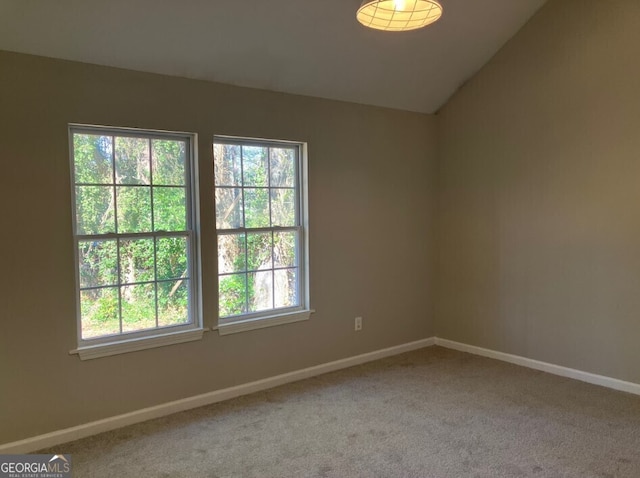 carpeted spare room featuring lofted ceiling and baseboards