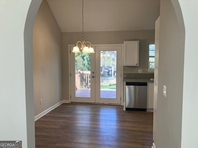 unfurnished dining area with dark wood-style floors, baseboards, vaulted ceiling, and arched walkways