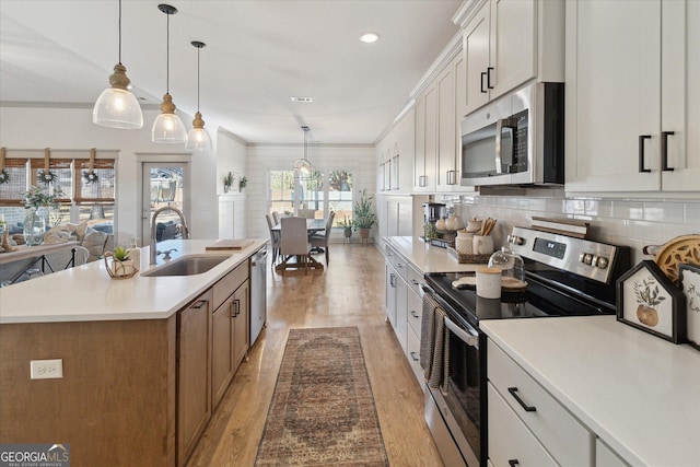 kitchen with stainless steel appliances, white cabinetry, hanging light fixtures, light countertops, and a center island with sink