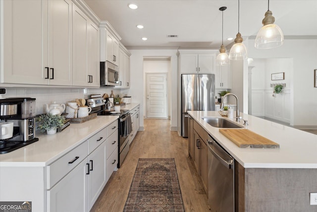 kitchen featuring light countertops, hanging light fixtures, appliances with stainless steel finishes, white cabinets, and a sink