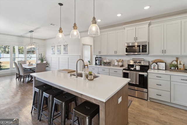 kitchen featuring pendant lighting, a center island with sink, light countertops, appliances with stainless steel finishes, and a sink