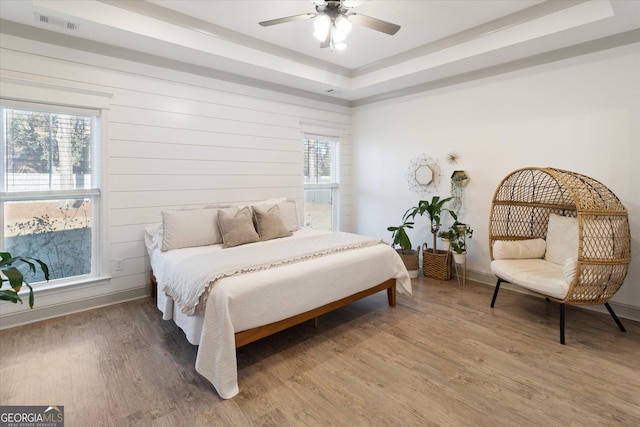 bedroom with wood finished floors, a ceiling fan, visible vents, baseboards, and a raised ceiling