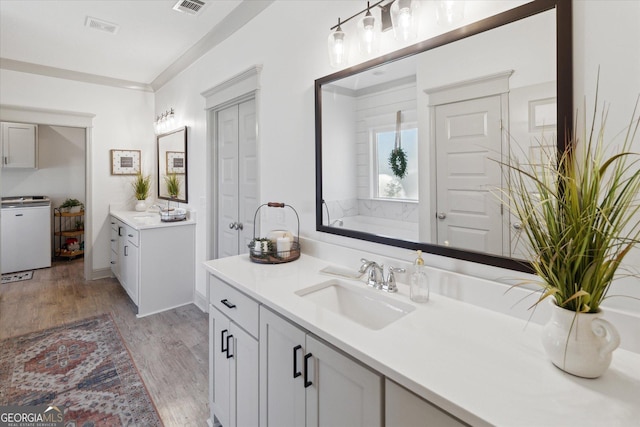 full bathroom featuring washer / dryer, wood finished floors, a sink, crown molding, and two vanities