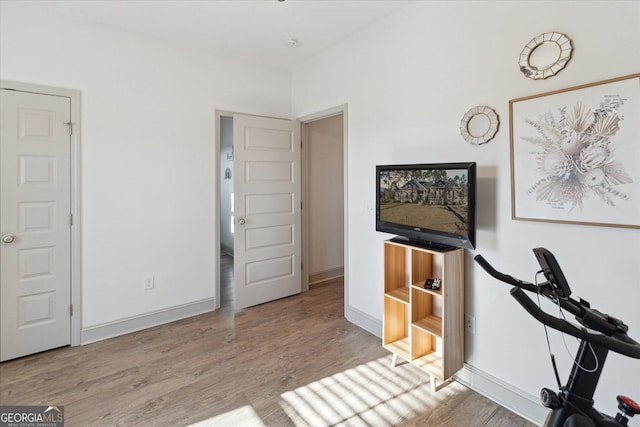 exercise room with baseboards and light wood-style floors