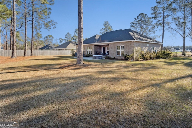 rear view of house featuring brick siding, a lawn, and fence