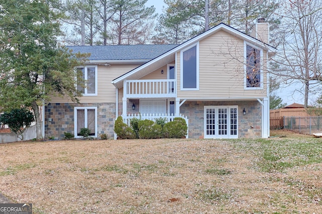 rear view of house featuring a balcony, fence, a yard, stone siding, and a chimney