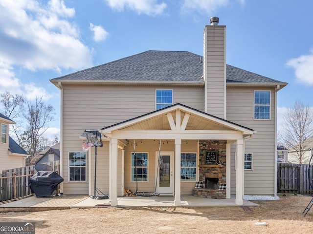 back of property with a shingled roof, a chimney, fence, an outdoor fireplace, and a patio area