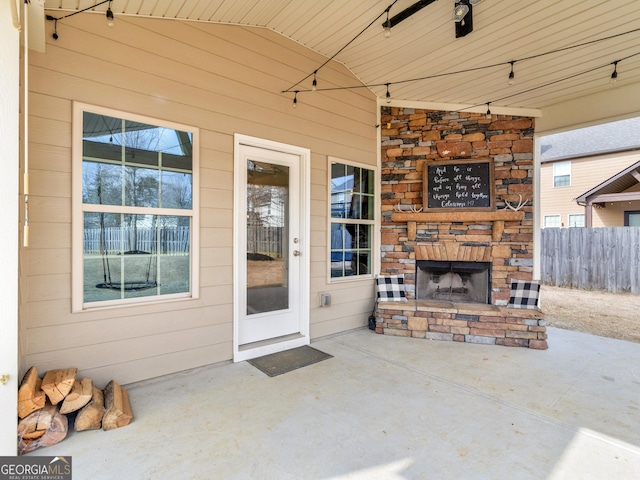 view of exterior entry featuring a patio, an outdoor stone fireplace, fence, a ceiling fan, and stone siding