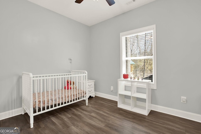 bedroom featuring a nursery area, visible vents, baseboards, and wood finished floors