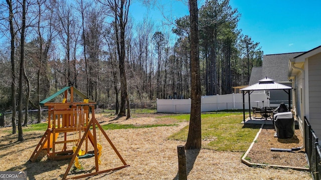 view of yard with a gazebo, a wooded view, a playground, and a fenced backyard