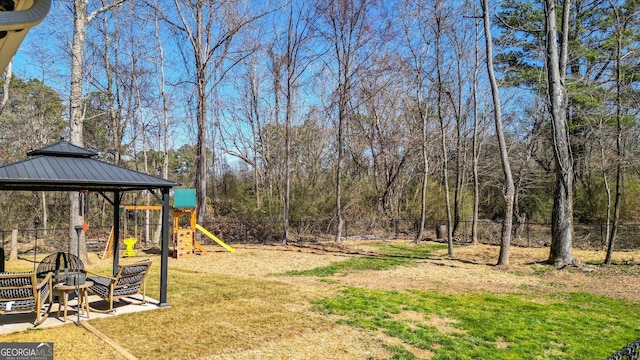 view of yard featuring a forest view, fence, a playground, and a gazebo