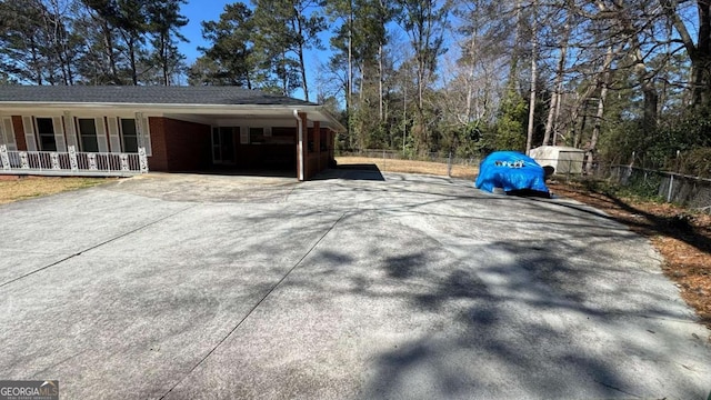 view of home's exterior with concrete driveway, fence, a porch, a carport, and brick siding