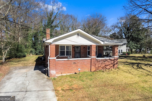 bungalow-style home with a porch, a chimney, a front lawn, and brick siding