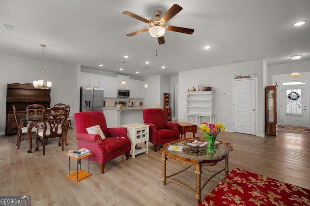 living area featuring light wood-style floors, visible vents, ceiling fan with notable chandelier, and recessed lighting