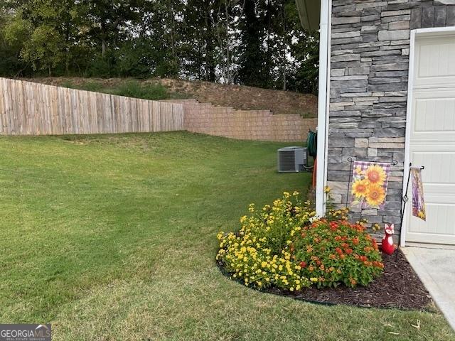 view of yard with a garage, a fenced backyard, and central AC