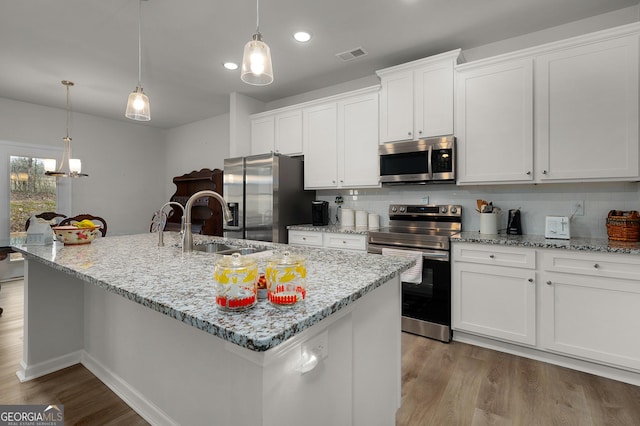 kitchen with stainless steel appliances, a kitchen island with sink, white cabinetry, and hanging light fixtures