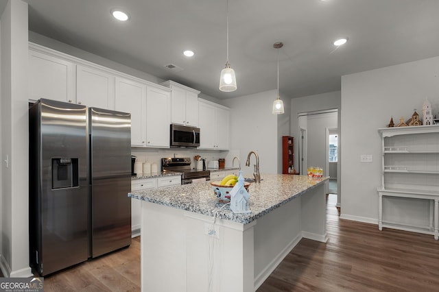 kitchen with appliances with stainless steel finishes, a center island with sink, white cabinetry, and pendant lighting