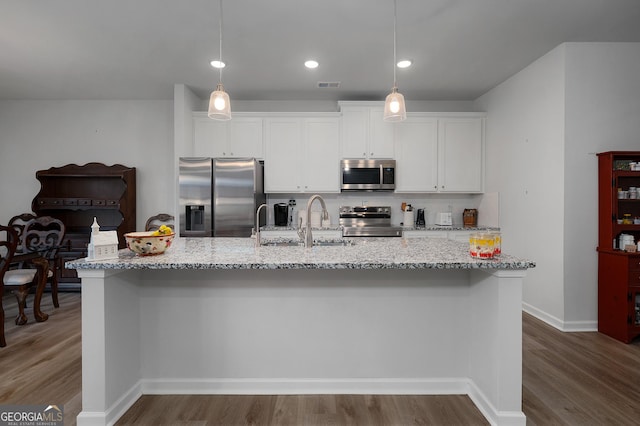 kitchen with a center island with sink, visible vents, white cabinets, appliances with stainless steel finishes, and decorative light fixtures