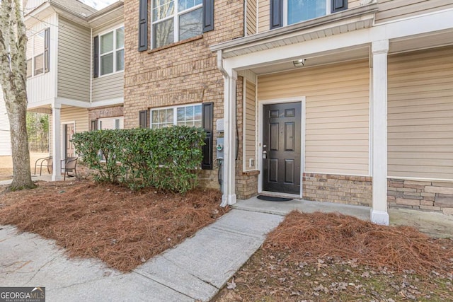 doorway to property featuring a porch, stone siding, and brick siding