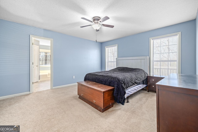 bedroom with light colored carpet, a ceiling fan, a textured ceiling, ensuite bath, and baseboards