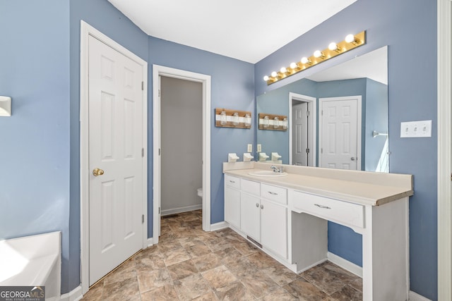 bathroom featuring toilet, a bathing tub, vanity, baseboards, and stone finish floor