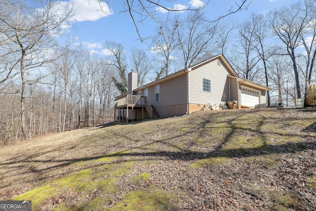 view of property exterior featuring a garage, a wooden deck, a chimney, stairs, and a yard