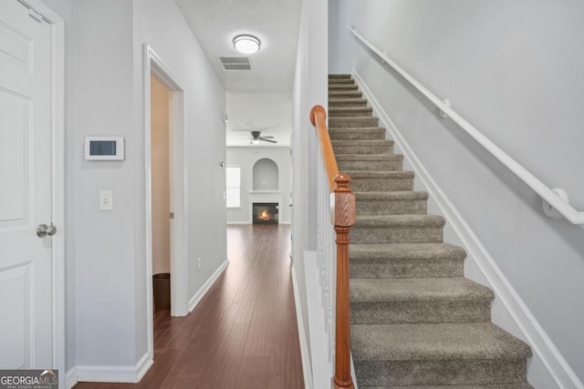 stairs with baseboards, visible vents, a glass covered fireplace, ceiling fan, and wood finished floors