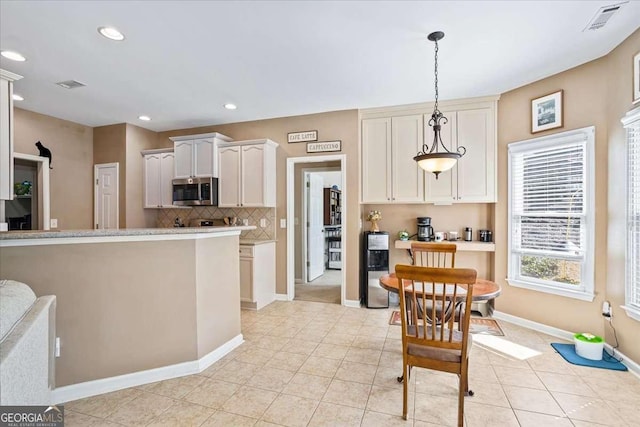 kitchen featuring pendant lighting, light countertops, stainless steel microwave, visible vents, and white cabinetry